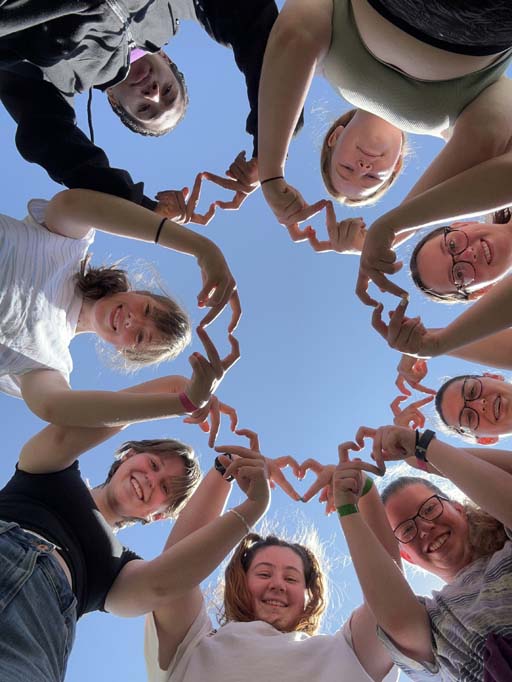 A group of girls standing over the camera in a circle and making heart shapes with their hands