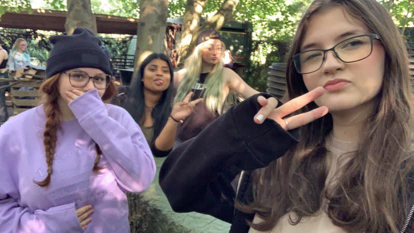 Four young women are taking a selfie. Charlotte is in the background wearing a backwards cap and two others are doing peace signs with their hands. 