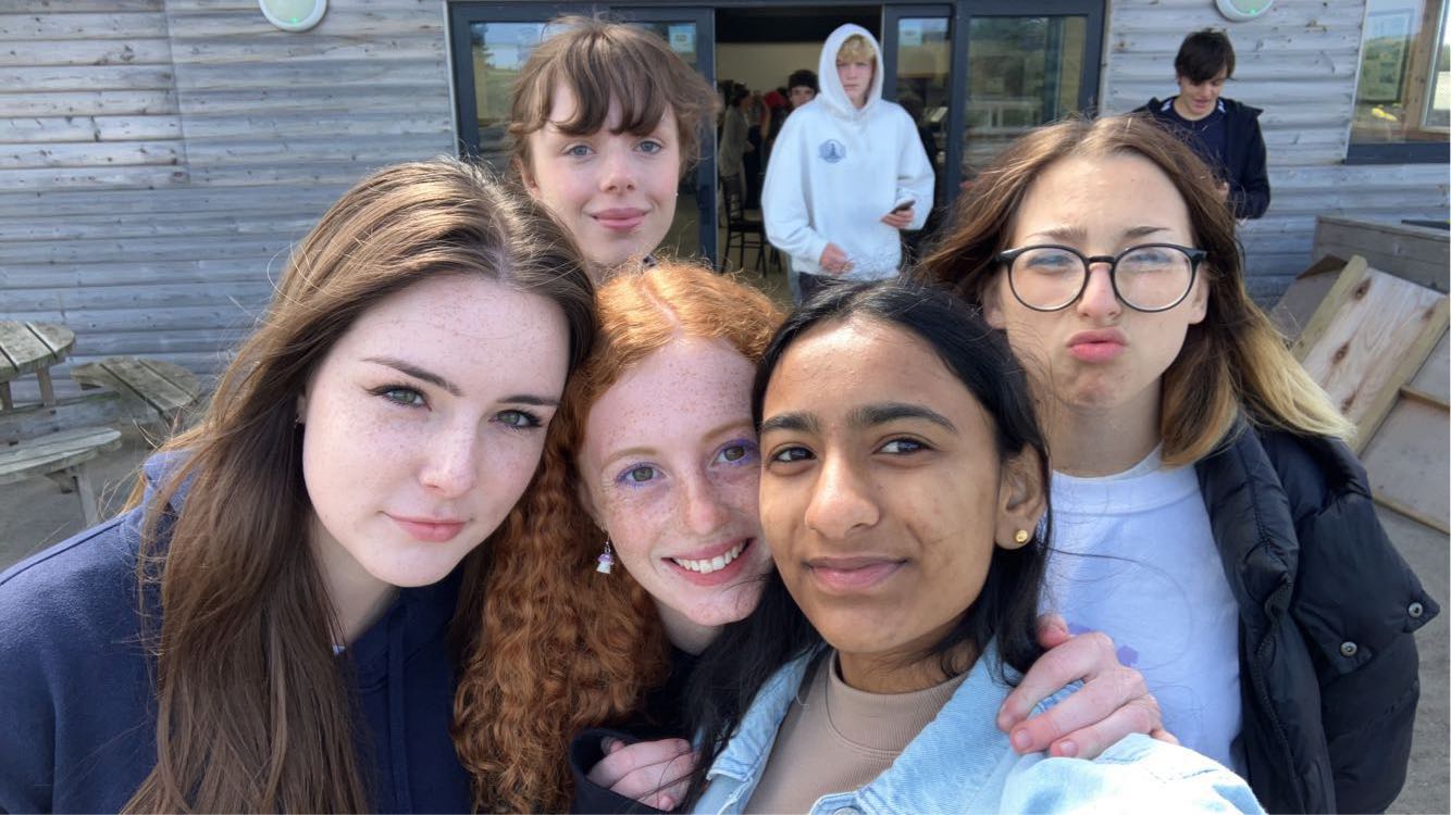 A group of five girls huddled closed together taking a selfie, Lilla is in the middle of the photo with curly red hair and wearing purple eyeshadow.