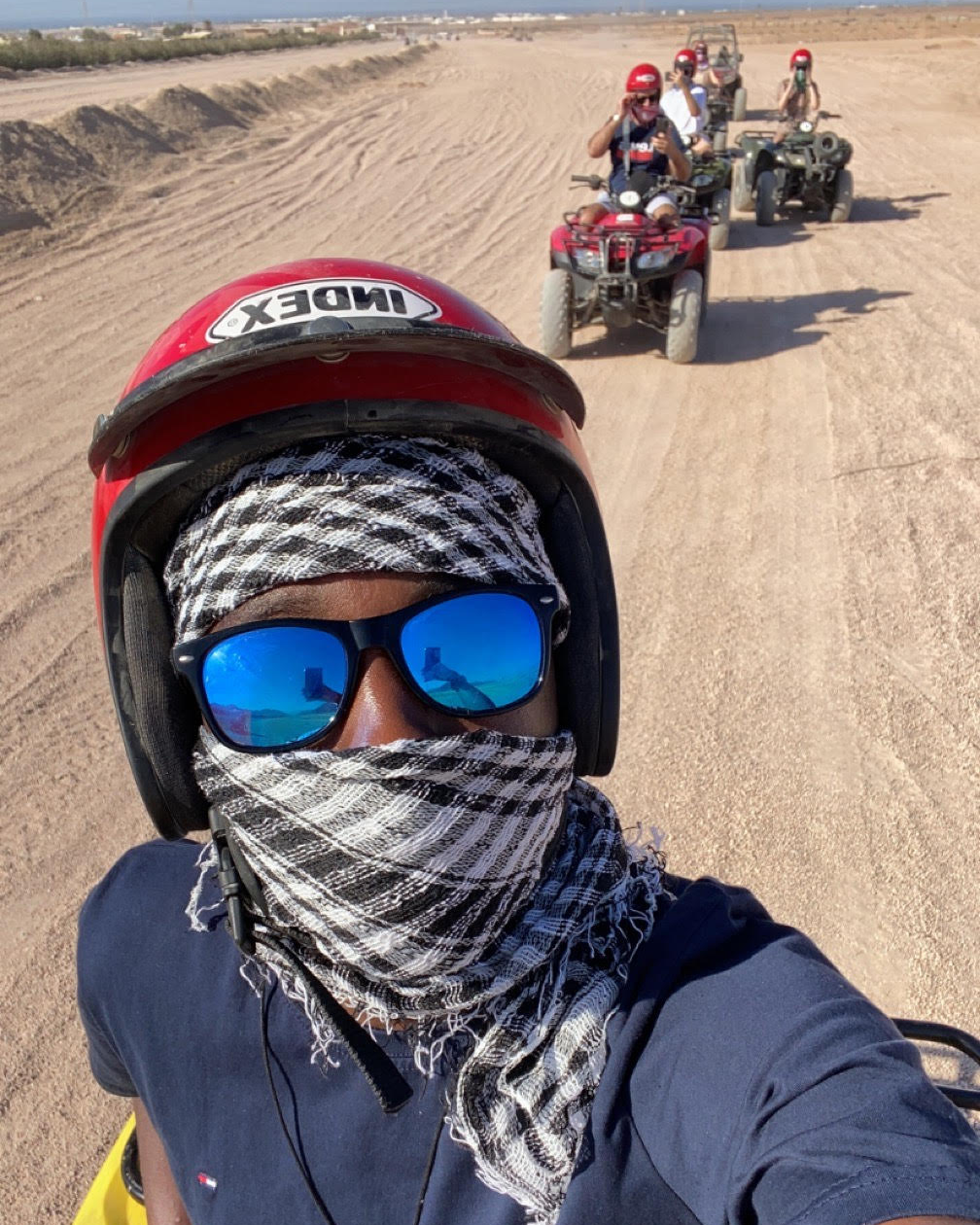  Ryan, riding a quad bike, wearing protective gear including a helmet and scarf with sunglasses navigates the terrain in Dubai Safari