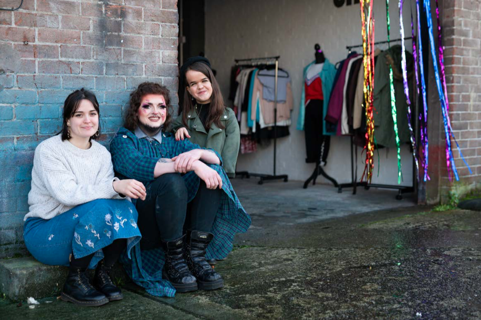 three young people sitting outside a swap shop