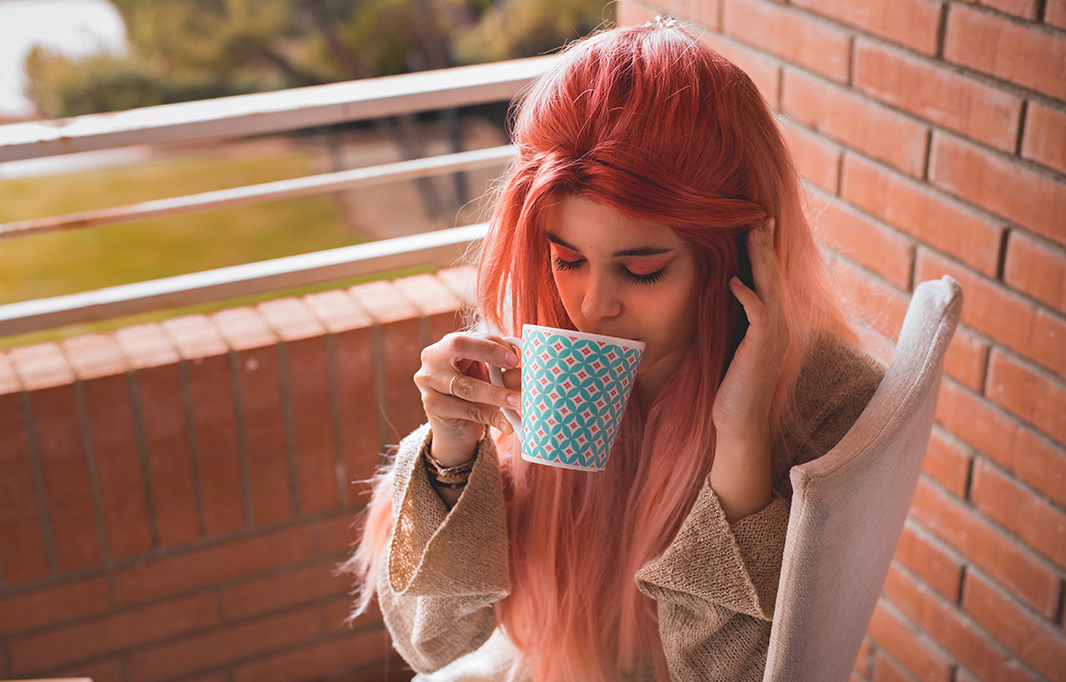 A woman with pink hair sitting on a chair holding a coffee mug
