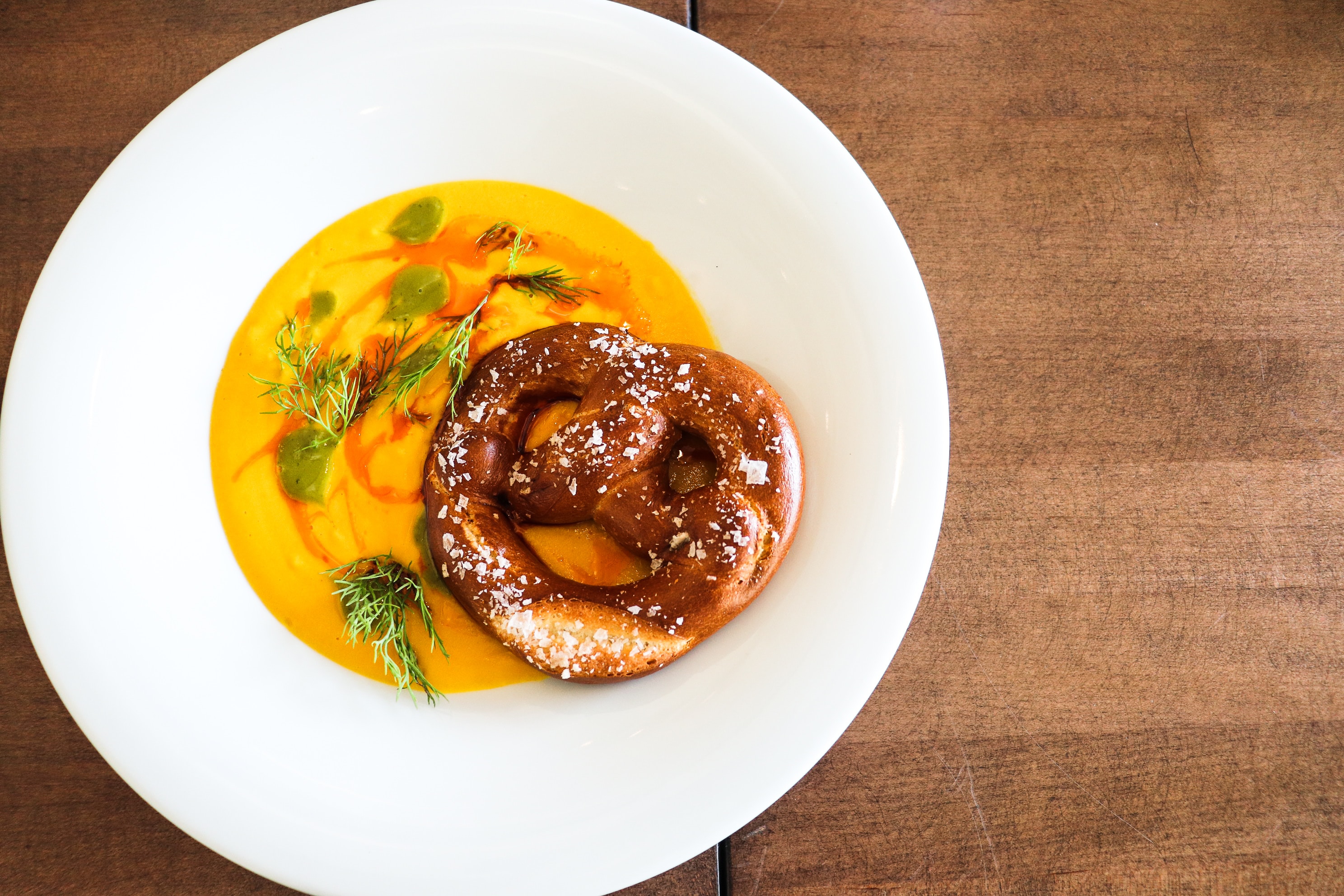  A pretzel placed on a pristine white plate, accompanied by Butternut Squash Soup