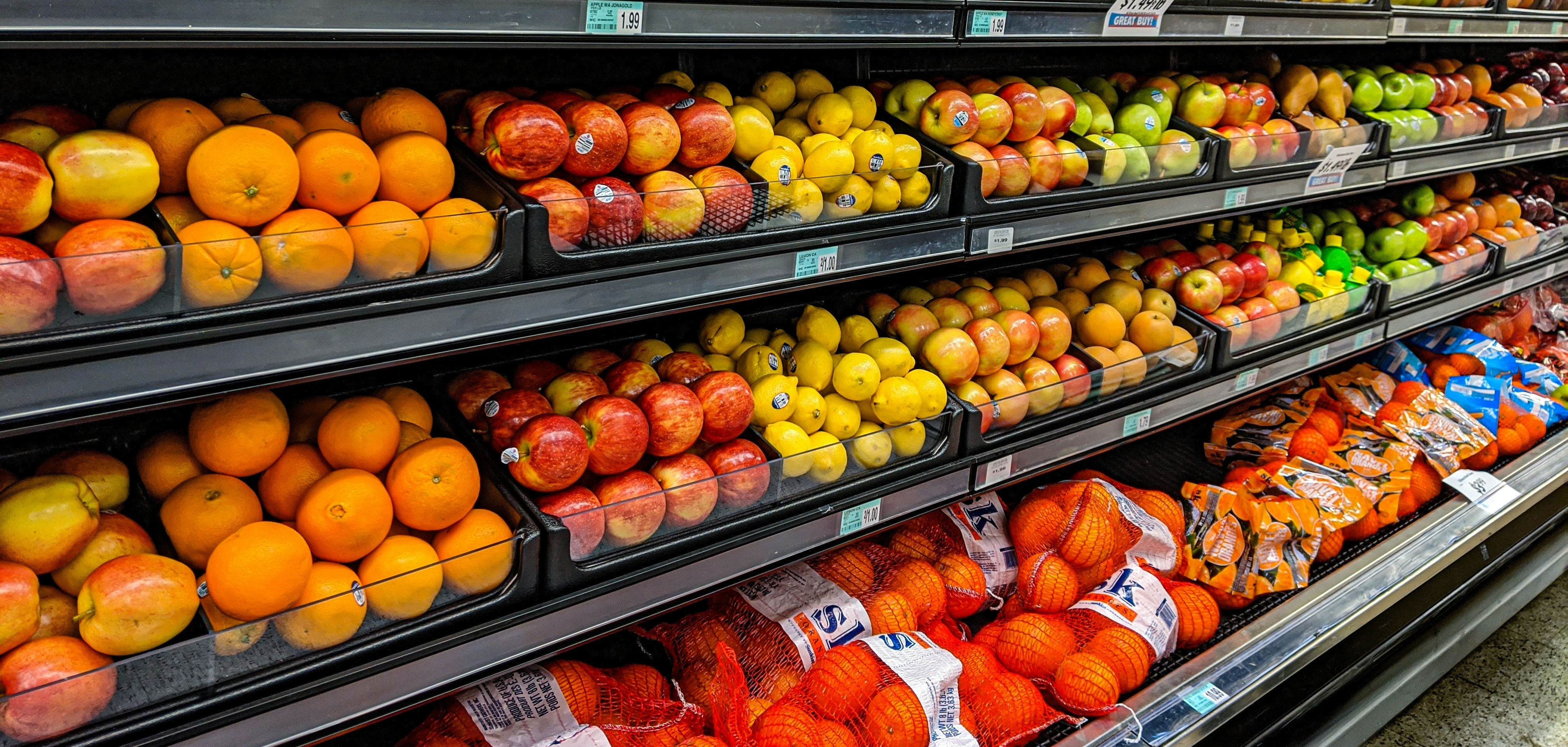 A fruit aisle in a supermarket, the shelves are filled with oranges, apples, limes and lemons.