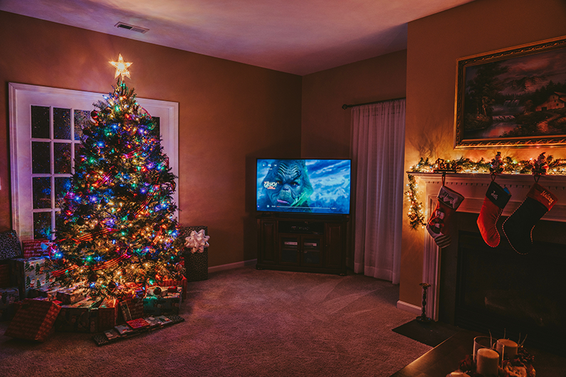 Inside a house with a Christmas tree, stockings hanging from a fireplace and the TV is on showing The Grinch.