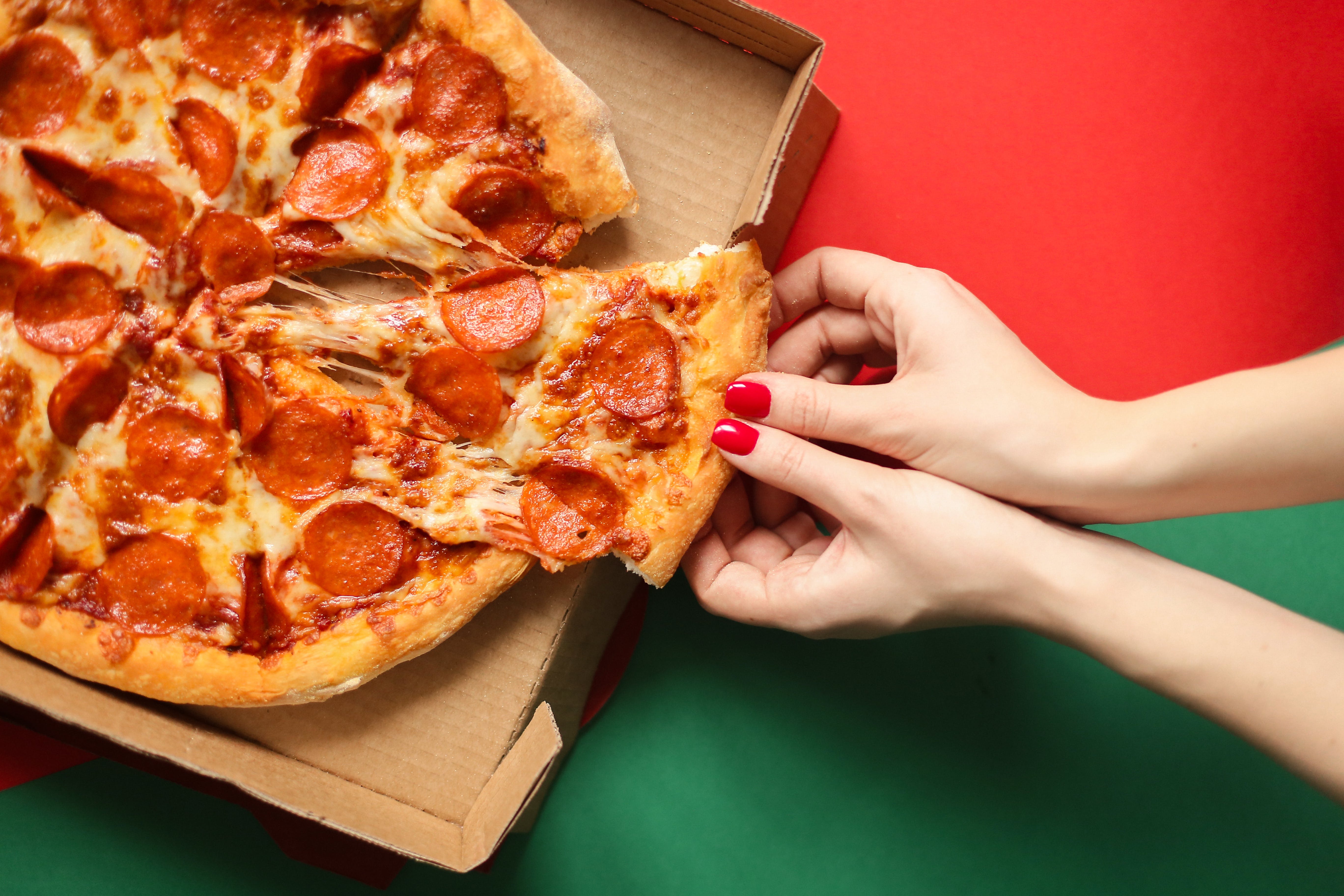 A pepperoni pizza in a takeaway box, with a slice being picked up by someone.