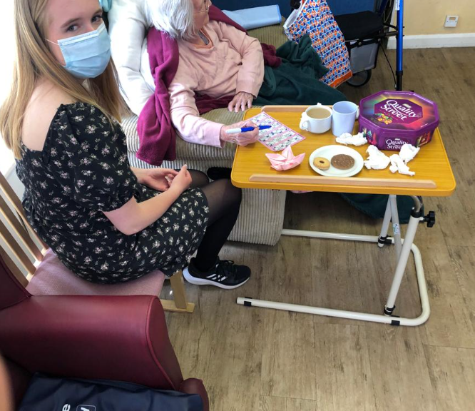 Young lady helping an elderly lady with bingo card in a care home.