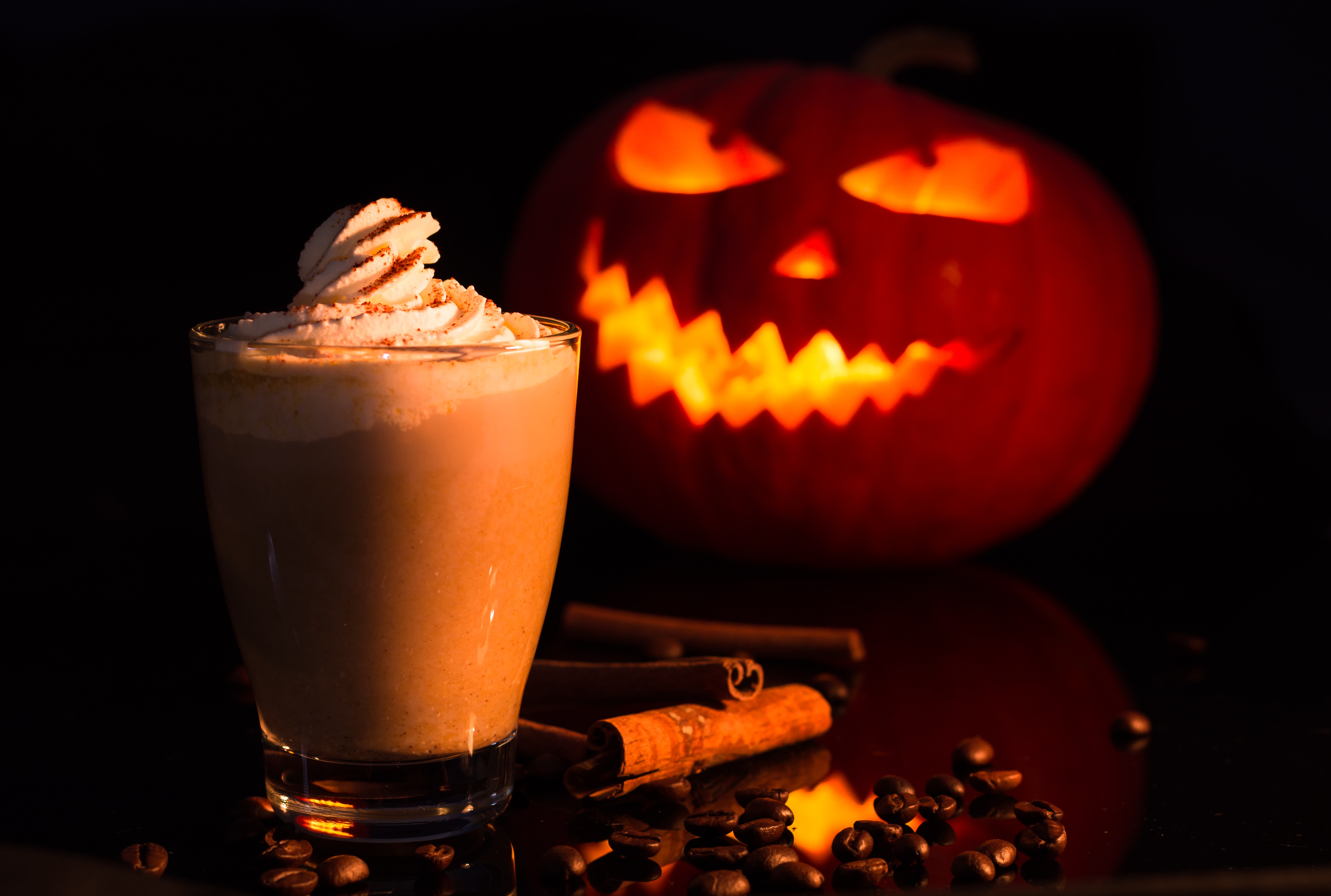 Halloween pumpkin spice latte drink with a lit orange carved pumpkin at the background