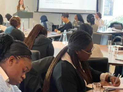 Jemimiah, a young black lady, is sat in a classroom with other students, she is writing in her notebook