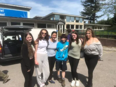 A diverse group of young girls gathered in front of a van, smiling and enjoying their time together outdoors.