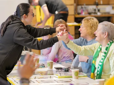 Summer wearing a black hoodie with glasses leaning forward with her hands up in a high five position. She is surrounded by elderly people.