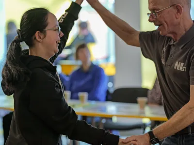 Summer wearing a black hoodie dancing with an elderly man in a grey shirt. 