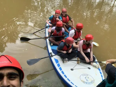 Team leader Uzair taking a selfie with a group of young people on a paddleboard in the water in the background. 