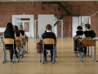 A group of students sat at desks which are spaced out in an exam hall setting.