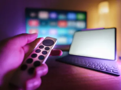 A hand holding a remote control pointing at a TV set 