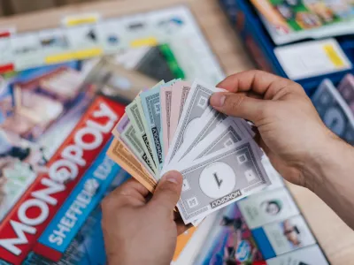 An individual holding Monopoly money while playing Monopoly on a table.