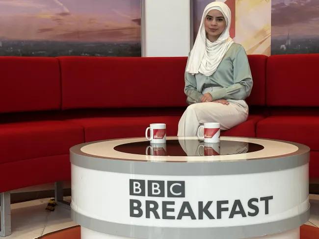 Shamza in a light green top and white hijab at the BBC Breakfast studio seated on a red sofa with two branded mugs on a table.