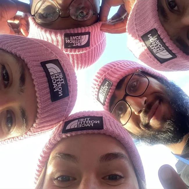 Five young people taking a closed up face selfie all wearing pink North Face beanies.