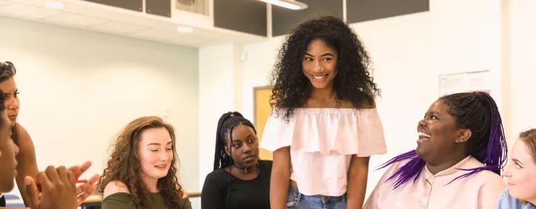 Young person standing at at table smiling talking with other young people