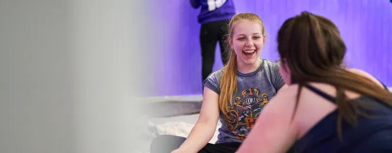 Young person sitting on floor laughing with another young person